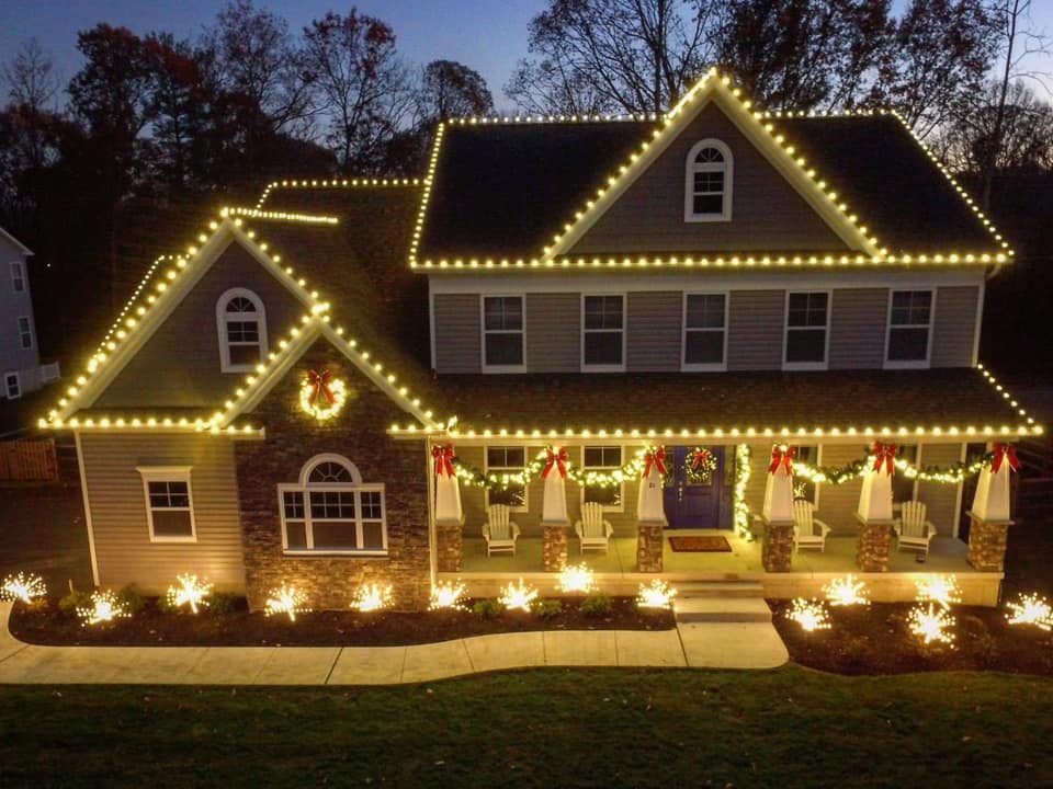 A two-story home with warm white lights along every peak and wreaths on the porch
